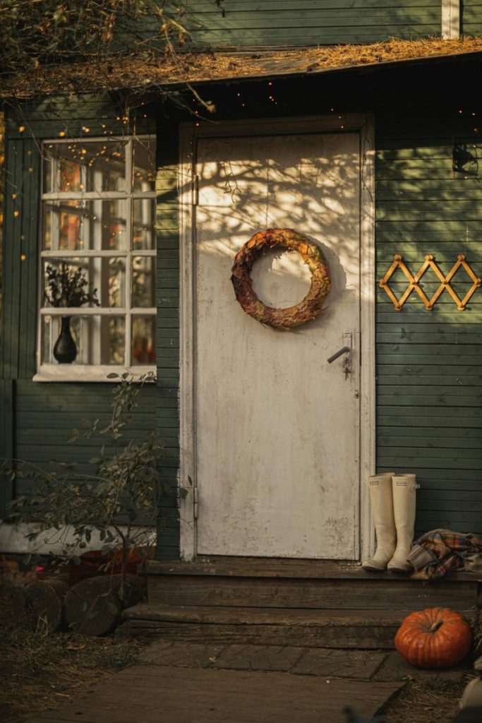 Charming rustic autumn scene with wreath, pumpkin, and boots by a vintage green house door.