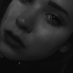 A close-up black and white portrait capturing a young woman's tearful expression, showcasing deep emotion and sadness.