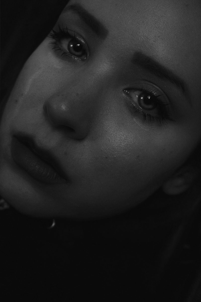 A close-up black and white portrait capturing a young woman's tearful expression, showcasing deep emotion and sadness.