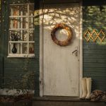 Charming rustic autumn scene with wreath, pumpkin, and boots by a vintage green house door.